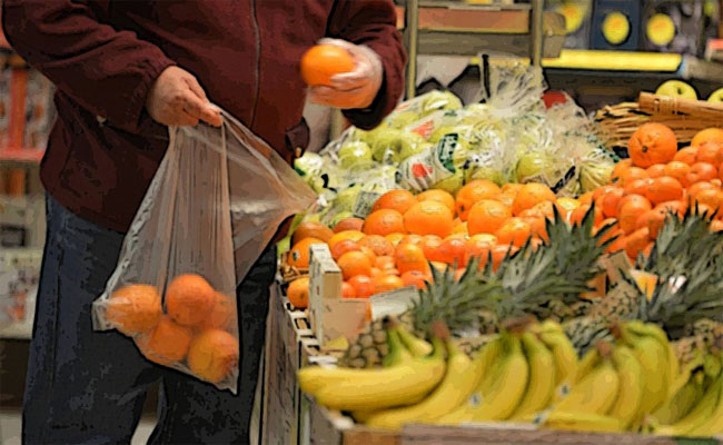 Un consumatore al supermercato infila arance in un sacchetto di plastica